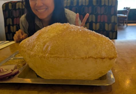 A giant loaf of bread in the foreground with the co-founder smiling and flashing a peace sign in the background